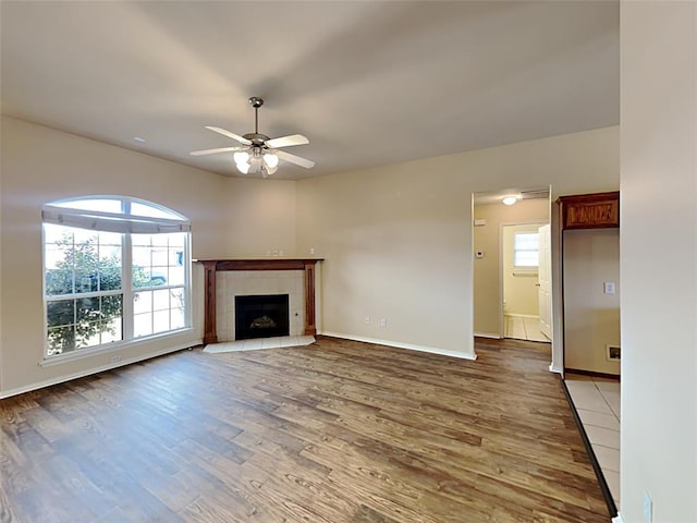 unfurnished living room with a fireplace, light wood-type flooring, baseboards, and a ceiling fan