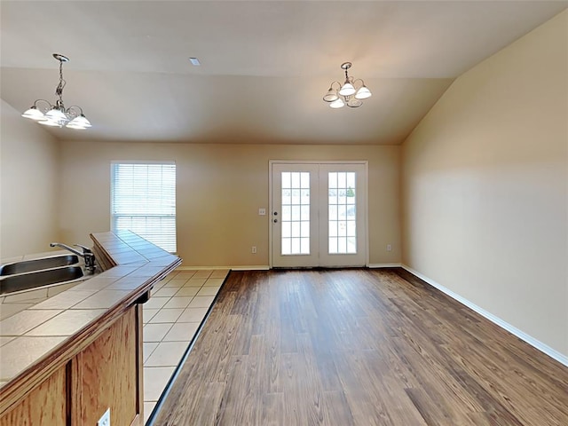 interior space featuring lofted ceiling, baseboards, an inviting chandelier, a sink, and wood finished floors