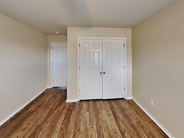 unfurnished bedroom with a closet, dark wood-type flooring, and baseboards