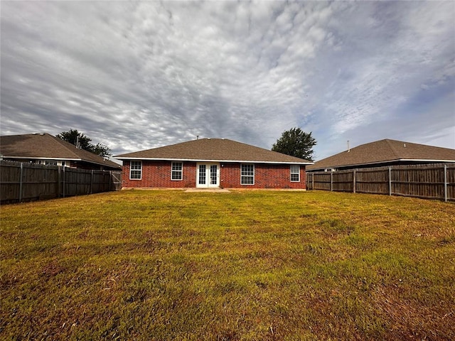back of house featuring a fenced backyard, french doors, brick siding, and a lawn
