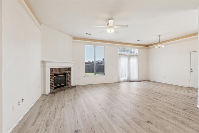 unfurnished living room with a brick fireplace, ceiling fan with notable chandelier, visible vents, and wood finished floors