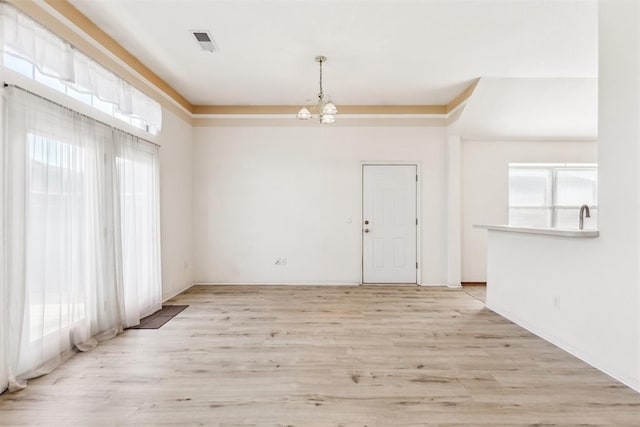 unfurnished room with light wood finished floors, an inviting chandelier, visible vents, and baseboards