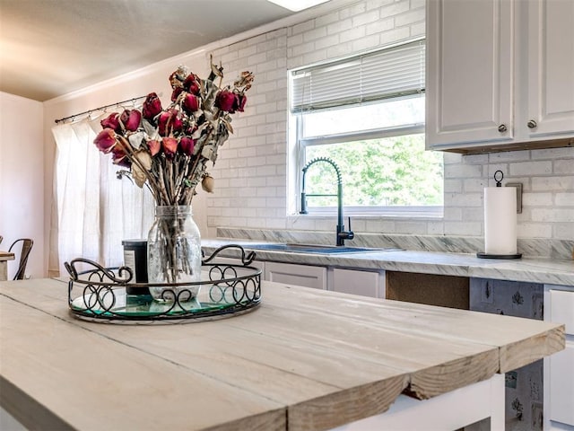kitchen featuring backsplash, light stone counters, white cabinets, and a sink