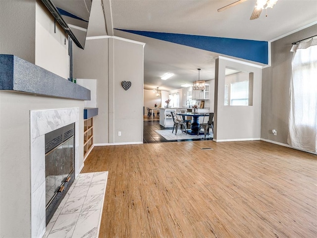 living area with a premium fireplace, vaulted ceiling, baseboards, ceiling fan with notable chandelier, and wood finished floors
