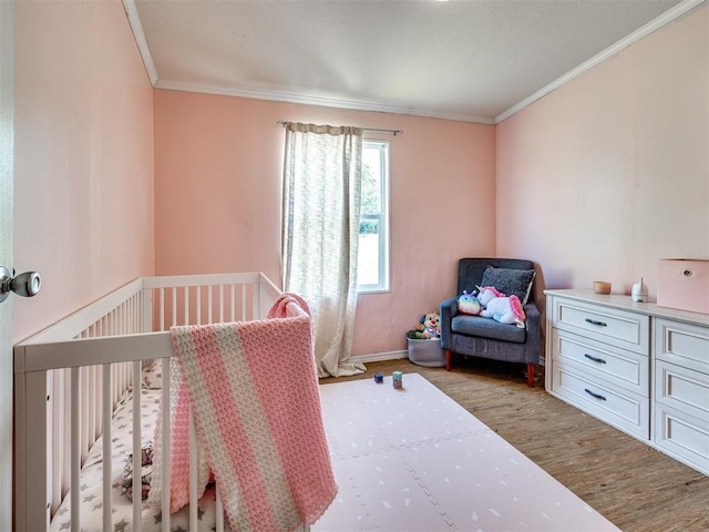 bedroom featuring baseboards, a nursery area, crown molding, and wood finished floors