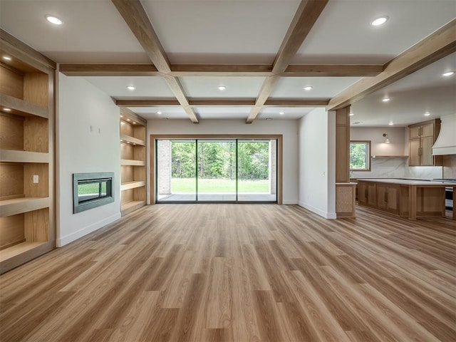 unfurnished living room with baseboards, coffered ceiling, plenty of natural light, light wood-style flooring, and a glass covered fireplace