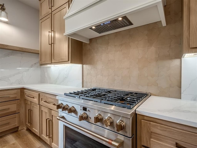 kitchen with high end range, custom exhaust hood, backsplash, light stone countertops, and light wood-style flooring