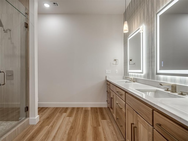 full bath with wood finished floors, a stall shower, double vanity, and baseboards