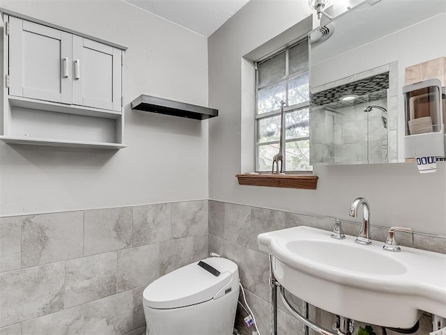bathroom with tile walls, tiled shower, toilet, a sink, and a wainscoted wall