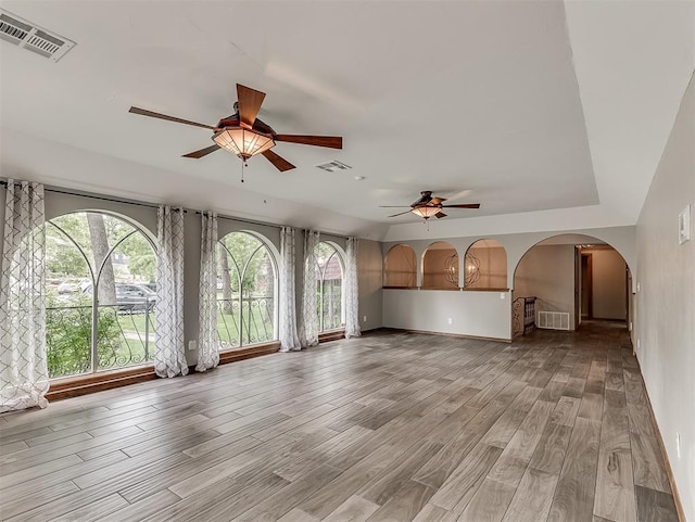 unfurnished living room featuring a ceiling fan, wood finished floors, healthy amount of natural light, and arched walkways