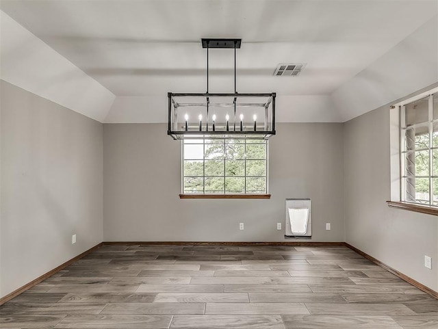 spare room with wood finished floors, a chandelier, and vaulted ceiling