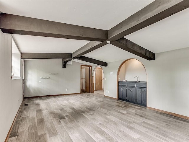 unfurnished living room with light wood-style flooring, beam ceiling, and arched walkways