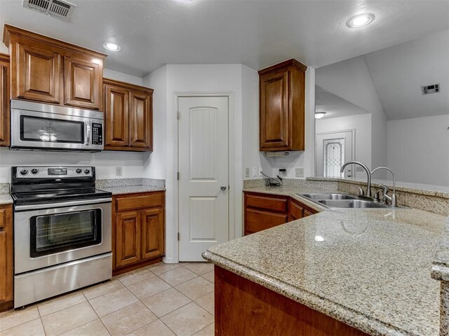 20140 N Rolling Meadows Dr, Luther, OK 73054 - kitchen featuring appliances with stainless steel finishes, a sink, brown cabinetry, light tile patterned floors, and a peninsula