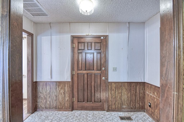 entrance foyer with tile patterned floors, a textured ceiling, visible vents, and wooden walls