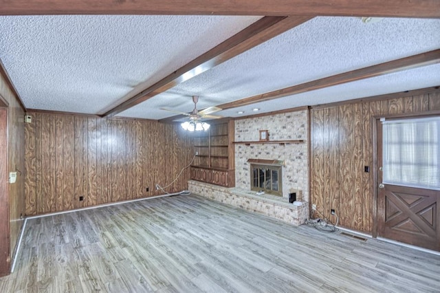 unfurnished living room with a textured ceiling, wooden walls, wood finished floors, and beam ceiling