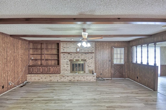 unfurnished living room with wooden walls, a textured ceiling, a ceiling fan, and wood finished floors