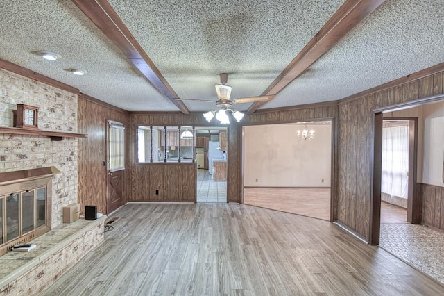 unfurnished living room featuring a fireplace, wood walls, wood finished floors, and ceiling fan with notable chandelier