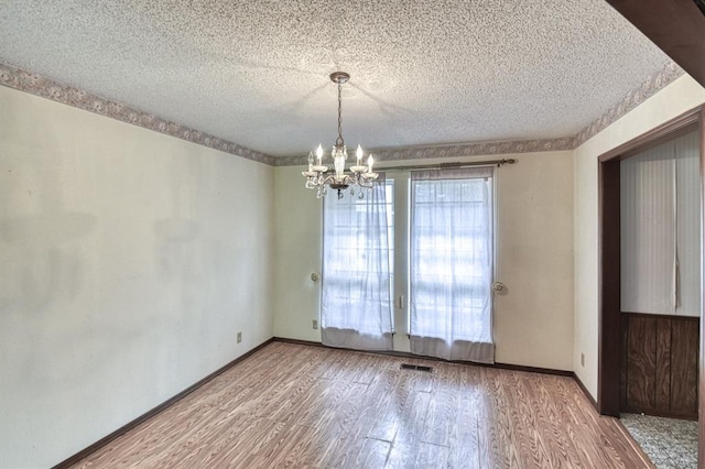 empty room with an inviting chandelier, visible vents, a textured ceiling, and wood finished floors