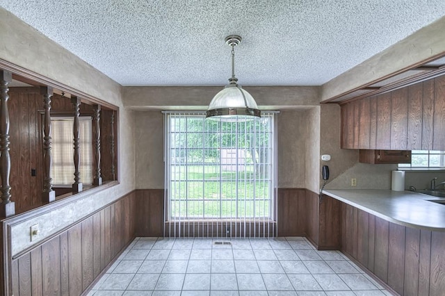 unfurnished dining area featuring wood walls, wainscoting, light tile patterned flooring, and a textured ceiling