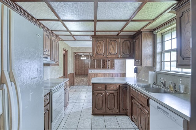 kitchen with a peninsula, a sink, white appliances, under cabinet range hood, and light countertops