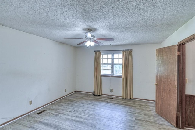empty room featuring a textured ceiling, visible vents, wood finished floors, and a ceiling fan