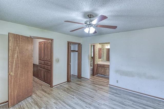 unfurnished bedroom with ensuite bathroom, a textured ceiling, baseboards, and wood finished floors