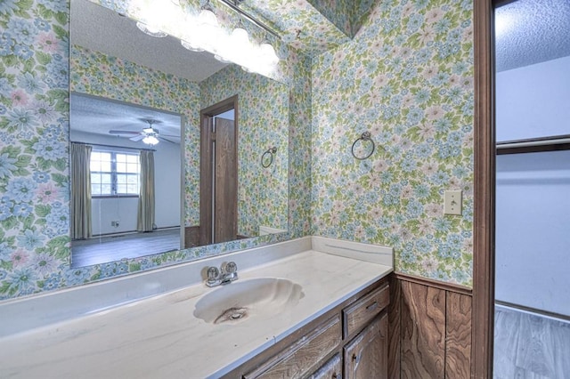 bathroom with vanity, a textured ceiling, and wallpapered walls