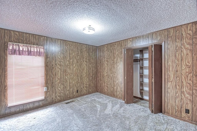 carpeted empty room with wood walls and a textured ceiling
