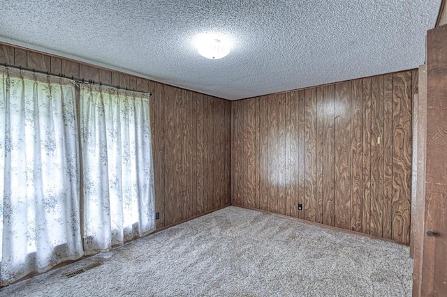 carpeted spare room featuring wood walls, a textured ceiling, and visible vents