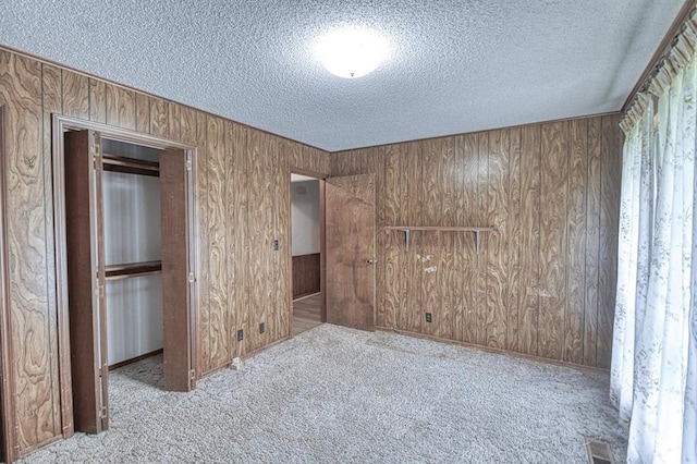 unfurnished bedroom featuring carpet floors, wooden walls, visible vents, and a textured ceiling
