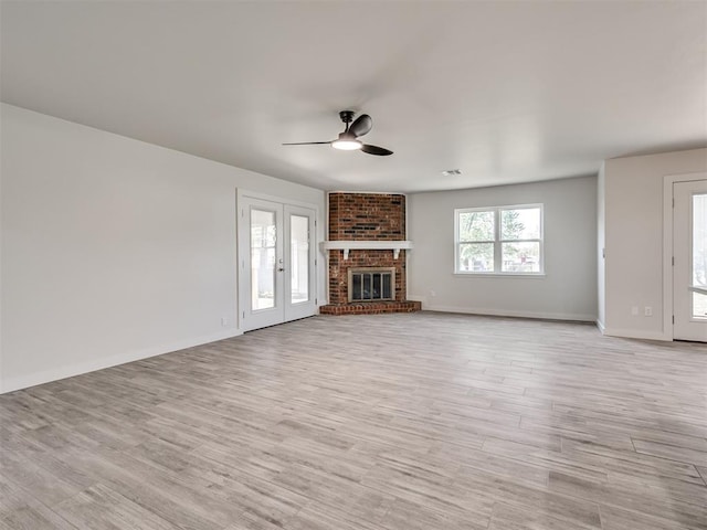 unfurnished living room with a ceiling fan, light wood-style flooring, a brick fireplace, and baseboards