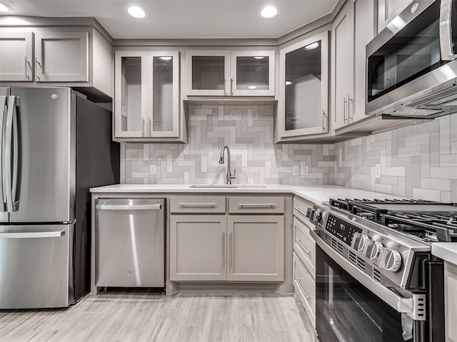 kitchen with appliances with stainless steel finishes, a sink, light countertops, decorative backsplash, and recessed lighting