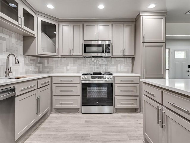 kitchen with stainless steel appliances, gray cabinets, a sink, light countertops, and recessed lighting