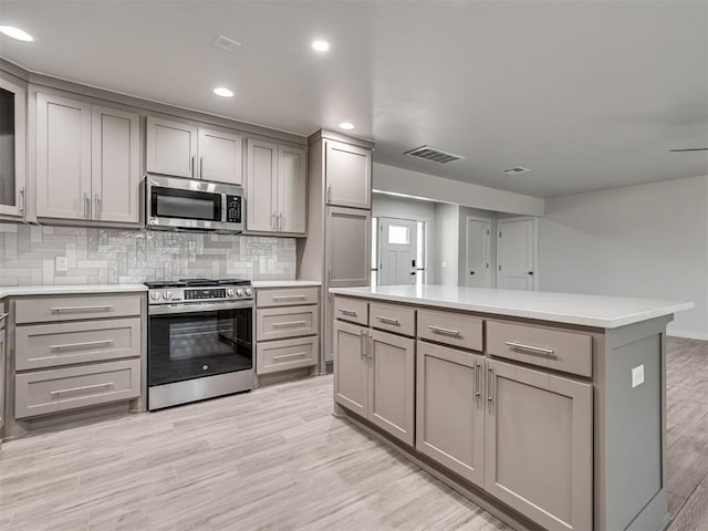 kitchen featuring appliances with stainless steel finishes, gray cabinets, backsplash, light wood-type flooring, and light countertops