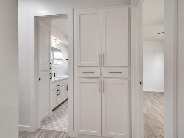 hall featuring baseboards, a sink, and light floors