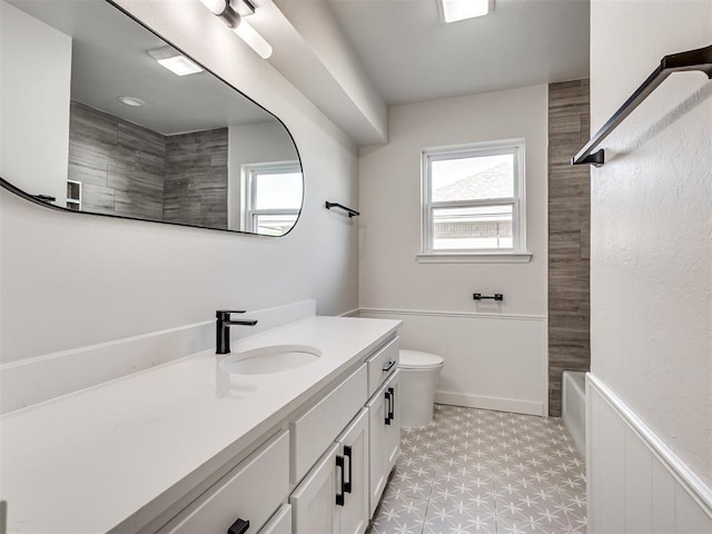 full bathroom with tile patterned floors, plenty of natural light, a wainscoted wall, vanity, and toilet