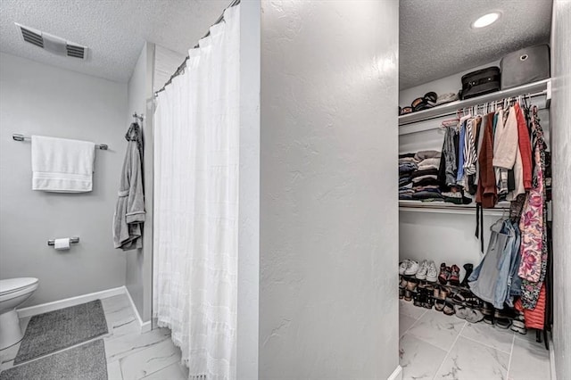 232 S Ranchwood Manor Dr, Oklahoma City, OK 73139 - full bath with marble finish floors, a textured ceiling, toilet, a walk in closet, and curtained shower