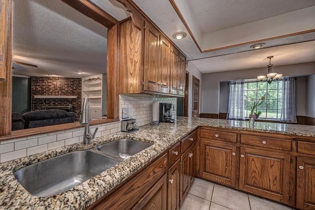 11125 NW 116th St, Yukon, OK 73099 - kitchen with a brick fireplace, a sink, a textured ceiling, brown cabinetry, and backsplash