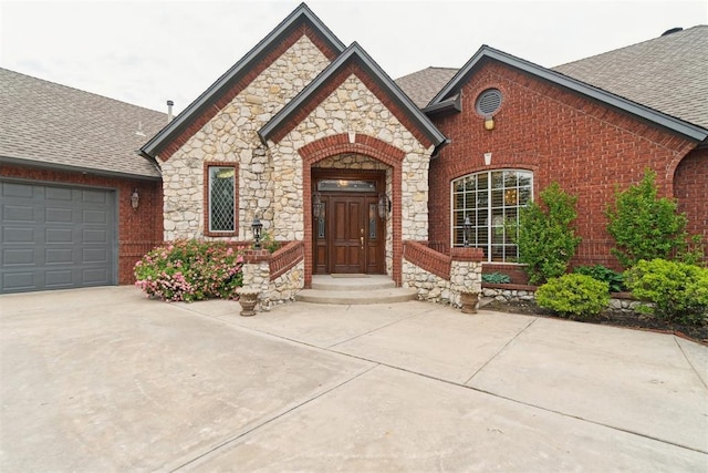 french country style house featuring roof with shingles, stone siding, concrete driveway, brick siding, and a garage