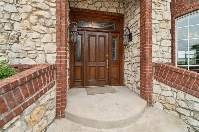 view of exterior entry with stone siding, covered porch, and brick siding
