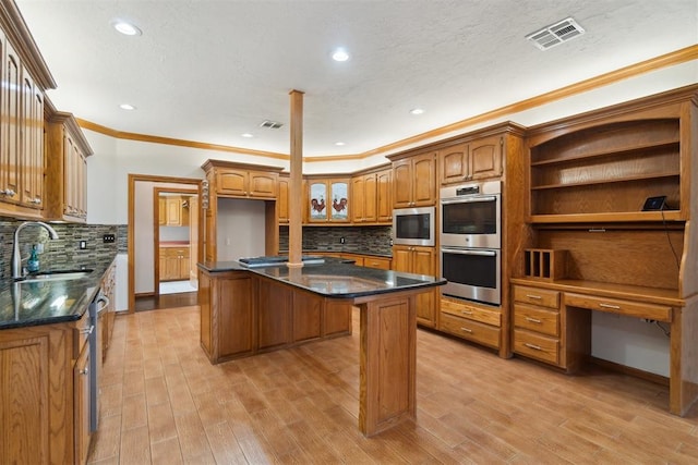 kitchen featuring a sink, appliances with stainless steel finishes, a kitchen island, crown molding, and brown cabinetry