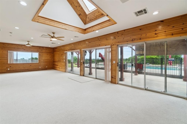 carpeted spare room with plenty of natural light, wood walls, recessed lighting, a skylight, and a ceiling fan