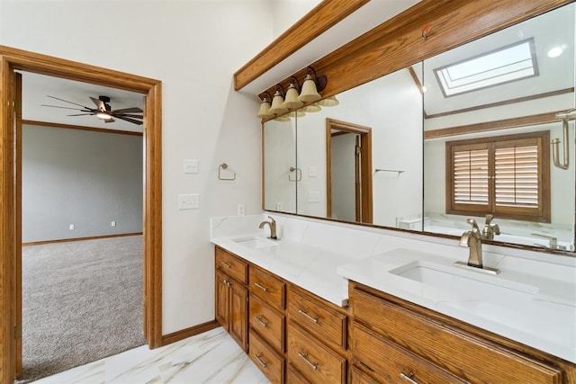 full bathroom with marble finish flooring, double vanity, a skylight, ceiling fan, and baseboards
