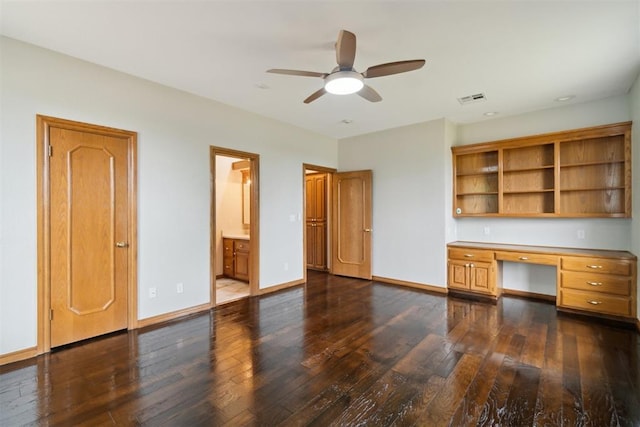 unfurnished office featuring built in desk, dark wood finished floors, a ceiling fan, and baseboards