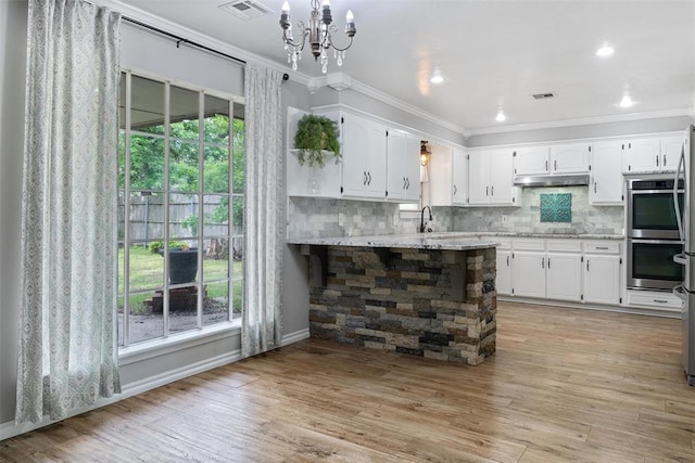 6408 Brentford Ter, Oklahoma City, OK 73132 - kitchen featuring ornamental molding, under cabinet range hood, double oven, white cabinetry, and a chandelier