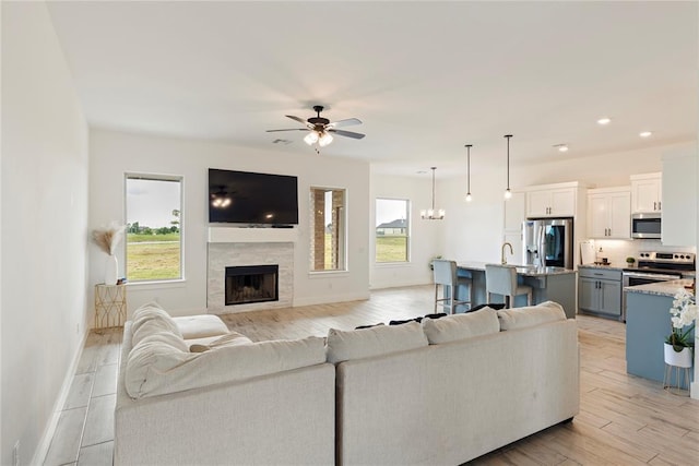 living area featuring a ceiling fan, baseboards, light wood-style floors, a tiled fireplace, and recessed lighting