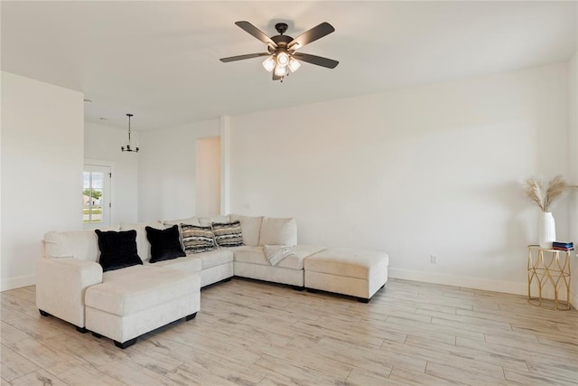 living area featuring light wood-style floors, baseboards, a ceiling fan, and a chandelier