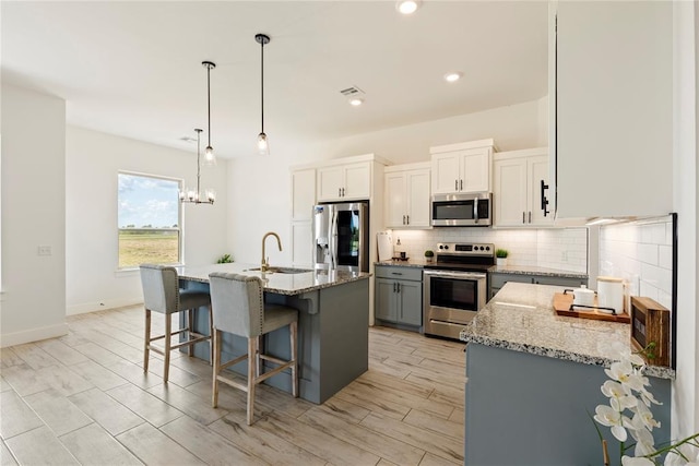 kitchen featuring stainless steel appliances, a sink, backsplash, light stone countertops, and a kitchen bar