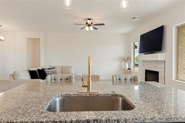 kitchen featuring open floor plan, a sink, a ceiling fan, and light stone countertops