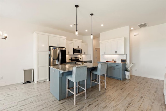 kitchen with appliances with stainless steel finishes, light wood-style flooring, a breakfast bar area, backsplash, and light stone counters